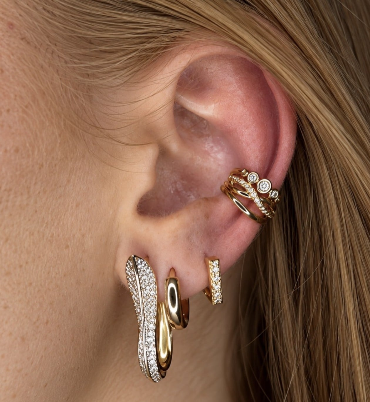 Primo piano dell'orecchio con ear cuff, cerchietti e orecchino a onda dorati
